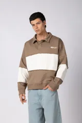 Buzo tipo polo de calce relajado con diseño de bloques de color en tonos marrón y blanco. Presenta cuello polo, cierre frontal parcial y logo estampado en el pecho. Confeccionado en tejido pesado con estructura.
