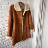 Gamulán largo de cuero color tostado con interior y detalles de corderito sintético en cuello y puños, cierre frontal de botones y bolsillos ribeteados.