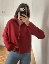 Sweater de punto color rojo con cuello polo, cierre frontal parcial con botones y detalle de costura en contraste a lo largo de la tapeta.