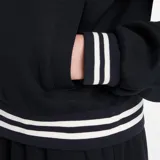 Campera deportiva New Balance negra con cierre frontal y cuello alto. Presenta puños y cintura con ribete de doble franja blanca. Lleva un pequeño logo bordado en el pecho.