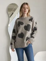 Sweater de punto en color beige con estampado de corazones negros, cuello redondo y mangas largas con puños acanalados.