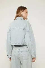 Campera cropped de denim celeste con tachas plateadas formando el logo de la marca.