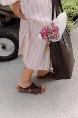 Bolso tipo tote de cuero marrón oscuro, con diseño minimalista, costuras reforzadas con remaches metálicos y correas largas para llevar al hombro.