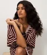 Vestido largo de viscosa con estampado geométrico en tonos bordó y blanco, escote en V y mangas cortas. Incluye un cinturón de cuerda para ajustar la cintura y una abertura frontal.