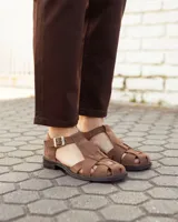 Sandalias de cuero gamuzado color marrón, tipo romanas, con tiras entrelazadas, talón cerrado y tira ajustable con hebilla metálica en el tobillo.