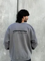 Buzo gris de corte oversize con cuello redondo y puños ajustados. Estampado en la espalda con la palabra "UNEXPECTED" y la frase "JOIN THE ROAD - POWER CONNECTION".