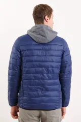 Campera capitoneada color azul marino, con capucha de algodón gris desmontable y cierre frontal. Tiene dos bolsillos exteriores con cierre.