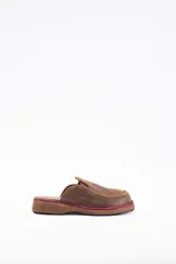 Zuecos de cuero vacuno color marrón, con diseño de punta redondeada y detalle de costura en el empeine. Presenta una suela plana con una franja decorativa en color bordó.