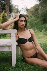 Conjunto de bikini negro con lunares color ladrillo, compuesto por un corpiño con aro, breteles regulables y espalda para atar, y una bombacha con tiritas laterales ajustables.