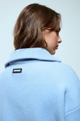Sweater de punto color celeste con cuello polo y cierre frontal parcial. Presenta detalles de terminación en color rojo en el cuello, puños y ruedo.