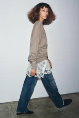 Jersey de punto fino en color marrón topo con escote en pico y manga larga. Presenta un diseño de doble capa con un bajo de encaje floral en color crudo que sobresale en la parte inferior.