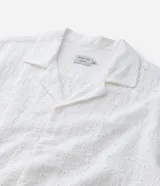 Camisa de hombre de calce holgado (comfort), confeccionada en algodón con técnica laise que incluye perforaciones florales cortadas con láser. Cuenta con cuello tipo solapa, manga corta y cierre frontal con botones al tono.