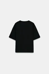 Camiseta de algodón compacto color negro, con cuello redondo, manga corta y detalle de aplique metálico en el frente que genera un ligero fruncido lateral.
