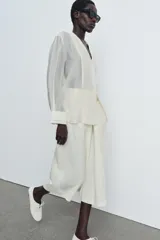 Camisa de mujer fluida de ZARA WOMAN COLLECTION, confeccionada en hilatura con mezcla de lyocell. Presenta escote en pico, manga larga con puños marcados y bajo asimétrico, con cierre frontal de botones ocultos.