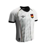 Camiseta de fútbol blanca con diseño geométrico sutil, cuello redondo negro y detalles en naranja. Presenta el logo de la FIFA World Cup 26 y el escudo de Alemania en el pecho.
