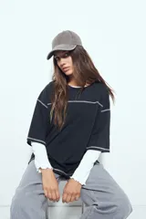 Remera de manga corta color marrón con efecto desgastado, corte oversize y costuras a la vista en color blanco. Presenta cuello redondo con cuello polo blanco superpuesto y mangas largas a rayas horizontales marrones y blancas por debajo.