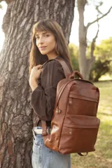 Mochila de cuero marrón, con compartimento principal amplio, bolsillo frontal con cierre y tiradores metálicos. Cuenta con correas regulables y diseño apto para notebook.