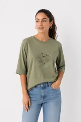 Remera de algodón color verde oliva con mangas 3/4 y cuello redondo. Presenta un diseño estampado frontal con detalles de strass y bordados.