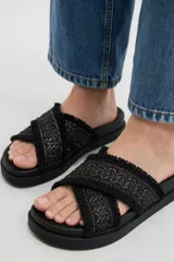 Sandalias planas color crudo con tiras cruzadas de tejido textil con diseño geométrico y detalles de flecos en los bordes.