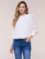 Blusa blanca de organza con textura devoré floral, silueta semiholgada y forro interno. Tiene escote bote, mangas largas abullonadas con transparencias, puños anchos con botones y ruedo elastizado.