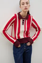 Buzo tipo polo de punto de algodón, con diseño de rayas verticales en rojo y crema. Presenta cuello y puños en color bordó, con cierre frontal de tres botones.