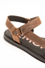 Sandalias planas de cuero marrón con tiras regulables mediante velcro y suela negra.