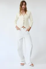 Chaqueta de punto color negro, con escote en pico, manga larga y cierre frontal con botones dorados. Presenta un diseño con bajo asimétrico.