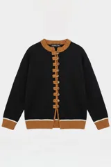 Saco tejido de punto en color negro, con detalles en color tostado en cuello, puños y ruedo. Presenta un cierre frontal con alamares y botones, y una línea blanca decorativa en los puños y el ruedo.