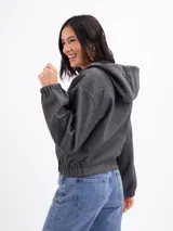 Campera de paño color beige con capucha, cierre frontal completo y mangas largas con puños elásticos. Presenta un diseño corto con ruedo elástico.