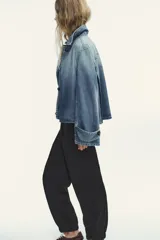 Pantalón negro de tiro medio con pinzas frontales, bolsillos laterales y falsos bolsillos de vivo en la espalda. El bajo termina en puño elástico.