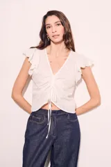 Blusa blanca de algodón con bordado broderie, escote en V con cordón ajustable, mangas cortas con volados y corte al cuerpo.