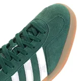 Championes Adidas Gazelle Indoor de gamuza color verde, con las icónicas tres tiras laterales en blanco y suela de caucho color caramelo. Presenta el nombre del modelo en letras doradas y detalle en el talón en color blanco.
