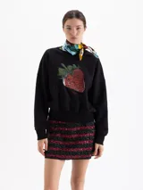 Buzo negro de corte holgado con cuello redondo, mangas largas y puños acanalados. Presenta un estampado central de una frutilla grande con detalles realistas.