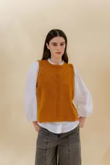 Chaleco tejido color mostaza con bordado artesanal en forma de V al tono. Tiene cuello redondo y sisas con sobretono.