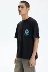 Remera de algodón negra, de corte holgado y diseño de hombros caídos. Presenta un pequeño estampado en el pecho con una flor celeste y el texto "KEEP THE WILD ALIVE".