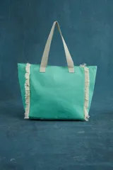 Bolso tipo tote color aguamarina, con flecos blancos en los laterales y asas de tela color beige.