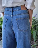 Pantalón de jean color beige, de corte recto y tiro alto, con ruedo deshilachado y cierre frontal con botón y cremallera.