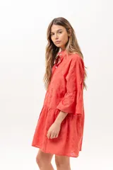 Vestido corto coral de broderie, con cuello camisero, cierre frontal de botones, mangas tres cuartos con volados y diseño escalonado en la falda.