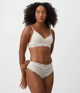 Bombacha caleçon femenina color blanco marfil, confeccionada en encaje floral con transparencia, cintura media, laterales anchos y bordes ondulados.