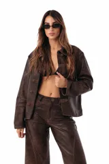 Campera estilo napoleón de cuero ovino color chocolate, con detalles de alamares y pespuntes en gamuza, y botones metálicos. Cuenta con cuello camisero, cierre frontal y mangas largas.