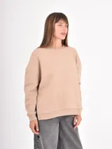 Buzo de cuello redondo, manga larga con puños elásticos y diseño holgado. Presenta un corte asimétrico con aberturas laterales en el ruedo.