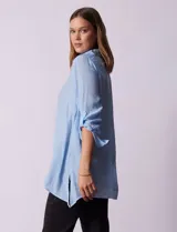 Camisa larga de rayón, con cuello clásico, cierre frontal con botones y mangas regulables con presilla. Presenta un diseño holgado con tajos laterales en el ruedo.