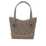 Bolso tote Crocs de color marrón claro, confeccionado en material sintético impermeable con perforaciones decorativas y funcionales para personalizar con Jibbitz. Presenta doble asa de hombro y el logo de la marca en relieve en el frente.