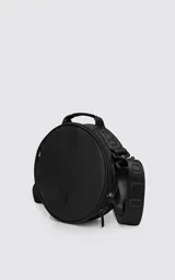 Bolso circular de estructura rígida, color negro, diseñado para el transporte de auriculares y accesorios. Cuenta con manija superior reforzada, correa de hombro ajustable con logo grabado, cierre perimetral y bolsillo trasero de acceso rápido.