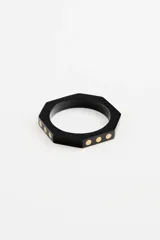 Pulsera rígida de resina negra con diseño octogonal y detalles de puntos metálicos dorados incrustados.