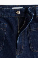 Jean de denim azul oscuro con tiro alto y piernas amplias de corte holgado. Cuenta con bolsillos delanteros de parche, cierre frontal con botón y raya marcada tanto en el frente como en la parte posterior.
