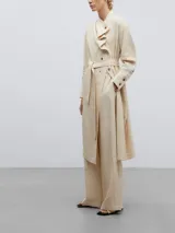 Vestido midi de lino y viscosa color beige, con cuello chal asimétrico, cierre frontal con botones, manga larga con puños abotonados, lazo ajustable en la cintura y tajos laterales en el ruedo.
