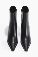 Botines de caña media con punta fina y taco fino tipo kitten heel. Presentan un diseño minimalista con costuras laterales visibles y cierre lateral.