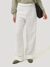 Pantalón de lino orgánico y viscosa, de color blanco y corte recto con tiro alto. Presenta detalles de calados sutiles en la cintura y en los dobladillos.