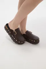 Suecos negros de estilo casual con acabado en eco cuero, detalle de hebilla metálica ajustable en el empeine y tachas decorativas en el contorno de la suela. Presentan una base de corcho y suela de goma dentada.